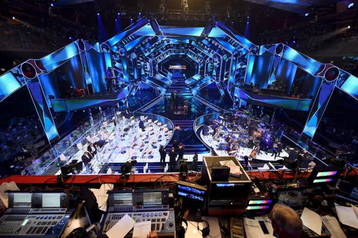 nella foto a colori si vede il palcoscenico del festival di Sanremo con luci blu e la postazione dell'orchestra ai lati dello stesso.