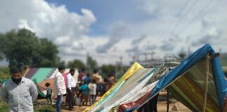 nella foto a colori si vede un campo con tende colorate, forse un campo profughi, con alcune persone di colore in piedi sulla sinistra. A destra, in primo piano, una tenda.