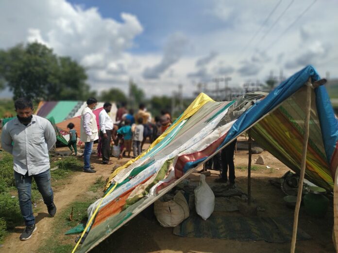 nella foto a colori si vede un campo con tende colorate, forse un campo profughi, con alcune persone di colore in piedi sulla sinistra. A destra, in primo piano, una tenda.