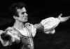 L'immagine è una foto in bianco e nero del celebre ballerino russo Rudol'd Nureev, inquadrato a bezzo busto di tre quarti, in costume e con le braccia aperte