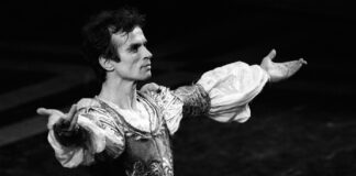 L'immagine è una foto in bianco e nero del celebre ballerino russo Rudol'd Nureev, inquadrato a bezzo busto di tre quarti, in costume e con le braccia aperte