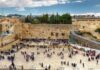 L'immagine è una foto di Gerusalemme, precisamente del Muro del pianto, ciò che resta dell'antico Tempio di Re Salomone. La piazza antistante il muro è popolata da numerosi fedeli e visitatori. Sullo sfondo si possono vedere i tetti della capitale israeliana tra cui la cupola dorata della moschea di Omar nella parte sinistra dell'immagine
