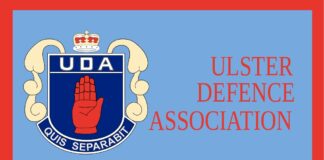 L'immagine mostra il logo della Ulster Defence Association, una mano rossa alzata su uno scudo blu contornato di bianco con una corona e la sigla UDA sopra ed il motto "Quis Separabit" sotto