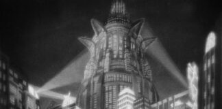 la foto in bianco e nero ritrae un edificio elevato e, intorno, altri edifici più bassi, sormontati da tre aloni luminosi