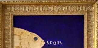 L'immagine mostra una delle opere di Sabatino della serie Pescibarocchi. Un piccolo quadro blu con un pesce giallo emergente dalla parte sinistra dell'immagine con al centro la scritta ACQUA illuminata. L'opera è contornata da una classica cornice in legno