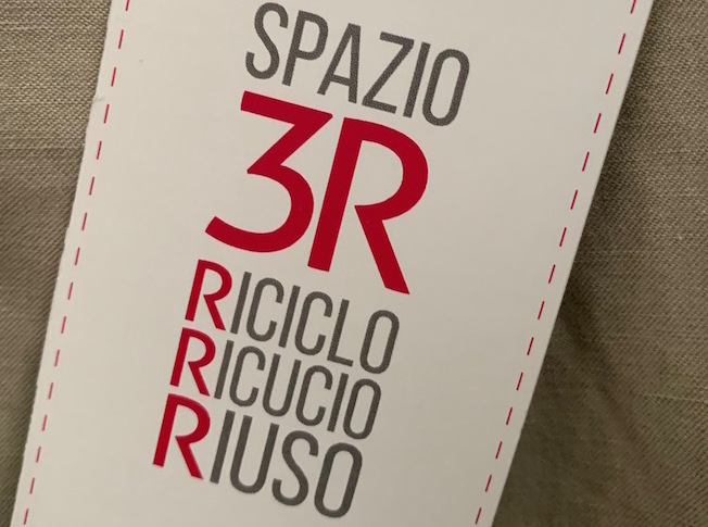 targhetta di un capo dell'Associazione Spazio3R Riciclo Ricucio Riuso, scritte in grigio e rosso su fondo chiaro