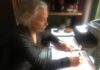 la foto a colori mostra la scrittrice Alda Mercante a scrivere su fogli di carta a mano sulla scrivania
