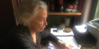 la foto a colori mostra la scrittrice Alda Mercante a scrivere su fogli di carta a mano sulla scrivania