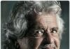 L'immagine mostra l'ex-comico e fondatore del Movimento 5 Stelle Beppe Grillo. Un uomo dai capelli bianchi e mossi sebbene corti con un accenno di barba bianca. La foto è a colori desaturati
