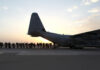la foto a colori mostra un aereo militare con militari in fila che stanno per entrare; la foto è stata scattata all'alba o al tramonto