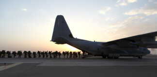 la foto a colori mostra un aereo militare con militari in fila che stanno per entrare; la foto è stata scattata all'alba o al tramonto