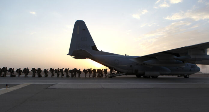 la foto a colori mostra un aereo militare con militari in fila che stanno per entrare; la foto è stata scattata all'alba o al tramonto