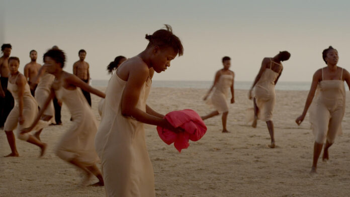 la foto a colori mostra alcune danzatrici di colore vestite di bianco; una di loro ha sulle mani un pezzo di stoffa rosso