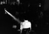 la foto in bianco e nero mostra un uomo girato di spalle che proietta un film di Pasolini