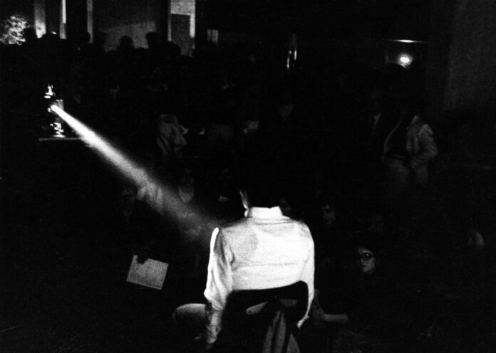 la foto in bianco e nero mostra un uomo girato di spalle che proietta un film di Pasolini