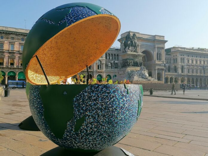 l globo è parte della mostra 100 globi per un futuro sostenibile All'interno di un contesto urbano c'è oggetto dalla forma sferica diviso a metà e con lo spicchio superiore sollevato verso l'alto