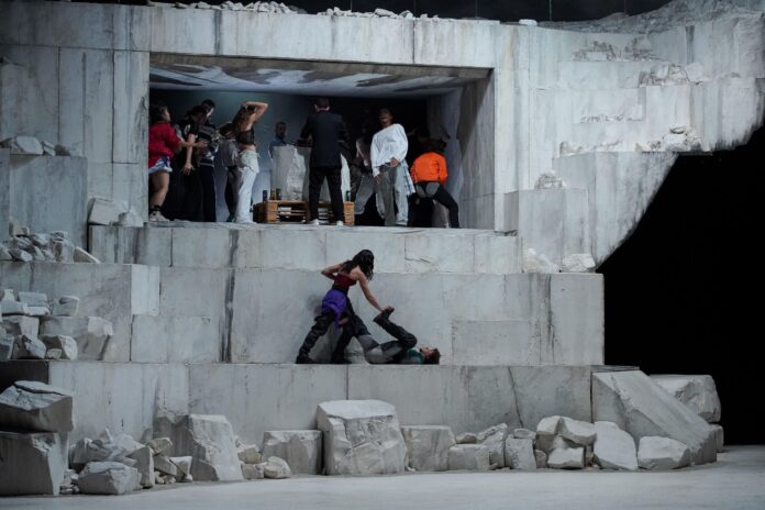 la foto a colori mostra un gruppo di ballerini che danzano all'interno di una coreografia fatta di grandi massi