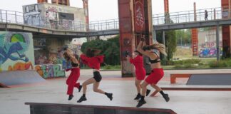 la foto a colori mostra quattro ballerine che danzano su un palcoscenico vestite in abiti sportivi neri e rossi, indossano infatti top e pantaloni corti da runner