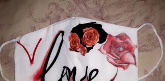 immagine di una mascherina bianca con la scritta love in rosso e nero. In alto e a destra della scritta ci sono delle rose, una più grande e tre più piccole su sfondo nero