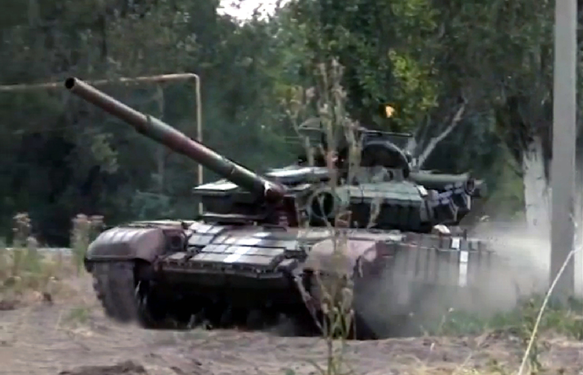 L'immagine mostra un carro armato durante l'assalto della Russia nella regione ucraina del Donbass. Il mezzo bellico avanza su un terreno polveroso con alcuni alberi nello sfondo