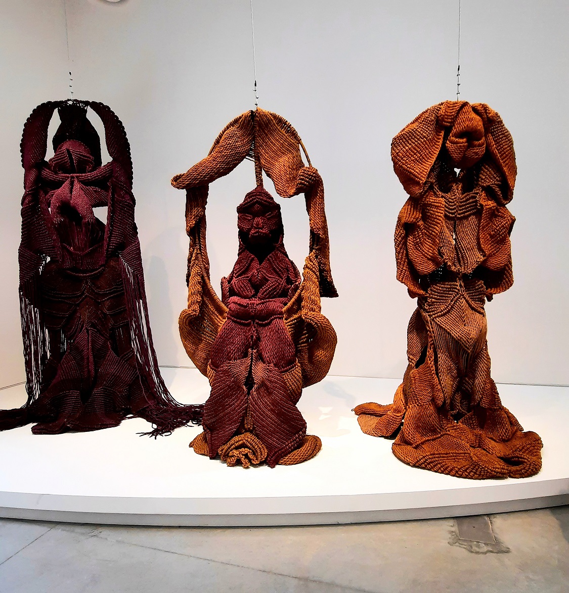 L'immagine mostra alcune delle opere dell'artista indiana Mrinalini Mukherjere attualmente esposte alla Biennale di Venezia 22. Si tratta di un gruppo di 3 statue fatte di tessuto grezzo dai toni rosso ocra vagamente simili a statue induiste, su uno sfondo bianco asettico